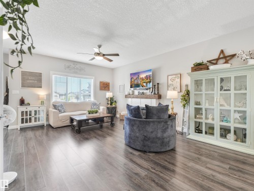 Spacious living area featuring wood-finish flooring, a ceiling fan with integrated lighting, and a large window with horizontal blinds - 283 Ameena Drive, Leduc, AB - Indoor Photo Showing Living Room