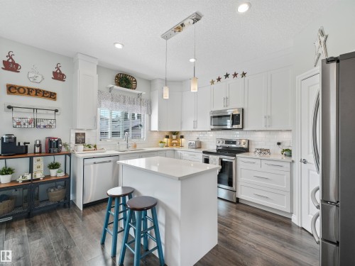 Modern kitchen featuring white shaker cabinetry, stainless steel appliances, a center island with countertop seating, subway tile backsplash, and wood-finish flooring - 283 Ameena Drive, Leduc, AB - Indoor Photo Showing Kitchen With Upgraded Kitchen