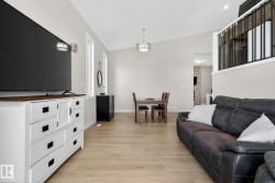 Open-concept living space featuring vaulted ceilings, light wood-finish flooring, a contemporary chandelier, and a black wrought iron railing - 