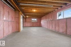 Unfinished lower level with concrete flooring, exposed wood joists, framed walls with pink insulation, two windows, and a white interior door - 