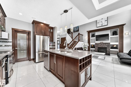 Gourmet kitchen featuring a central island with integrated sink, stainless steel appliances, white tile flooring, and dark wood cabinetry - 16244 138 Street Nw, Edmonton, AB - Indoor Photo Showing Kitchen With Double Sink With Upgraded Kitchen