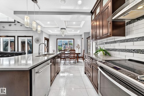 Gourmet kitchen featuring a large island with sink, stainless steel appliances, dark wood cabinetry, a tile backsplash with decorative accents, and recessed and pendant lighting - 16244 138 Street Nw, Edmonton, AB - Indoor Photo Showing Kitchen With Double Sink With Upgraded Kitchen
