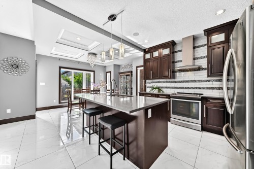 Spacious kitchen featuring dark wood cabinetry, stainless steel appliances, and a central island with countertop seating - 16244 138 Street Nw, Edmonton, AB - Indoor Photo Showing Kitchen With Upgraded Kitchen
