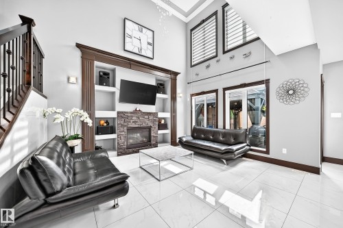 Living room featuring a stacked stone fireplace with an integrated entertainment center, white tile flooring, and high ceilings - 16244 138 Street Nw, Edmonton, AB - Indoor With Fireplace