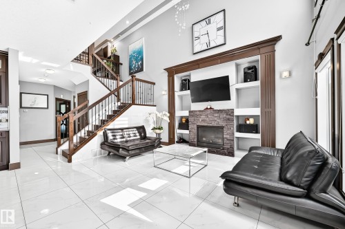 Spacious living area featuring polished tile flooring, a two-story ceiling, and an ornate dark wood staircase with wrought iron balusters - 16244 138 Street Nw, Edmonton, AB - Indoor With Fireplace
