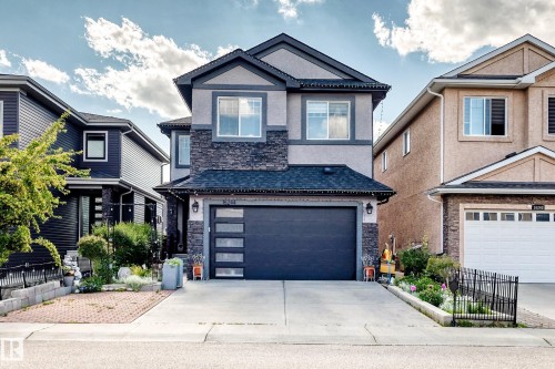 Two-story stucco and stone exterior featuring a dark gray garage door with frosted glass panels, an asphalt shingle roof, and a concrete driveway - 16244 138 Street Nw, Edmonton, AB - Outdoor With Facade