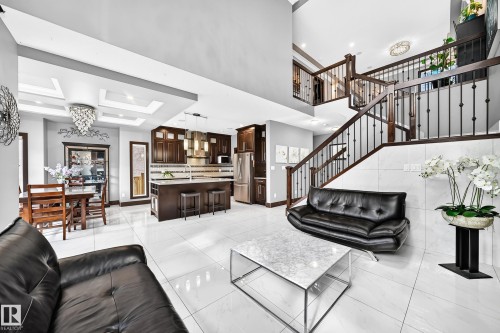 Spacious open-concept living area featuring white tile flooring, a two-story ceiling, and a prominent staircase with dark wood railings and black spindles - 16244 138 Street Nw, Edmonton, AB - Indoor