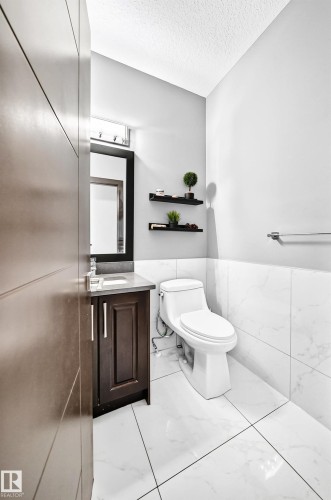 Contemporary powder room featuring large format white tile flooring, white subway tile wainscoting, and a dark wood vanity with a light-colored countertop - 16244 138 Street Nw, Edmonton, AB - Indoor Photo Showing Bathroom