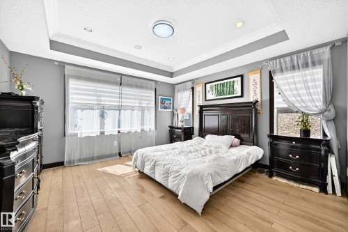 Spacious room featuring wood-finish flooring, tray ceiling with recessed lighting, and multiple windows - 16244 138 Street Nw, Edmonton, AB - Indoor Photo Showing Bedroom