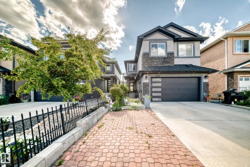 Two-story stucco and stone-clad residence featuring a modern garage door with frosted glass panels, a concrete driveway, and a paved walkway - 16244 138 Street Nw, Edmonton, AB - Outdoor