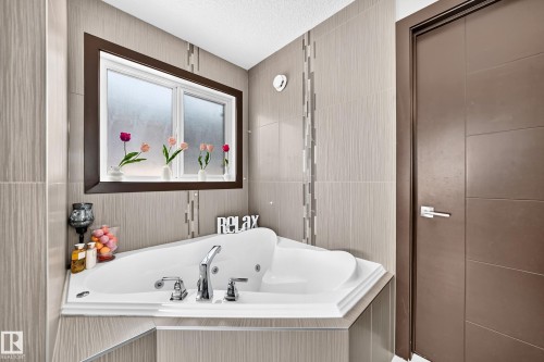 Corner jetted bathtub with chrome fixtures, surrounded by large format tile walls featuring decorative vertical tile accents - 16244 138 Street Nw, Edmonton, AB - Indoor Photo Showing Bathroom