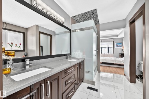 Dual vanity with integrated sinks, a wide framed mirror, and a contemporary light fixture - 16244 138 Street Nw, Edmonton, AB - Indoor Photo Showing Bathroom