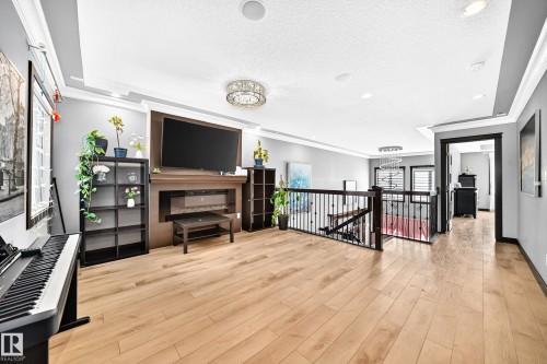 Spacious upper-level landing featuring wood-finish flooring, a built-in electric fireplace with an integrated media center, recessed lighting, and an open staircase with a wrought-iron railing - 16244 138 Street Nw, Edmonton, AB - Indoor Photo Showing Other Room
