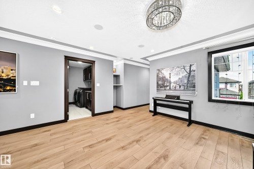 Spacious room featuring wood-finish flooring, light gray walls with dark trim, and a decorative ceiling light fixture - 16244 138 Street Nw, Edmonton, AB - Indoor