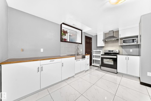 Kitchen featuring white cabinetry, stainless steel appliances, wood-finish countertops, tile flooring, and a subway tile backsplash - 16244 138 Street Nw, Edmonton, AB - Indoor Photo Showing Kitchen
