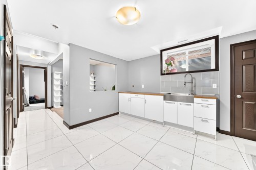 Utility space featuring large format white tile flooring, a stainless steel farmhouse sink, wood-finish countertops, white cabinetry, and grey tile backsplash - 16244 138 Street Nw, Edmonton, AB - Indoor Photo Showing Other Room