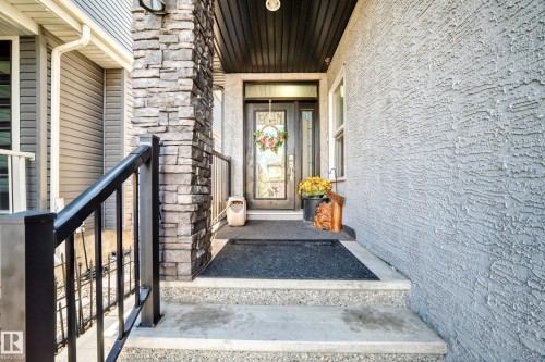 Front entrance featuring a dark-paneled door with decorative glass inserts, a stone-clad pillar, and a textured stucco exterior - 16244 138 Street Nw, Edmonton, AB - Outdoor