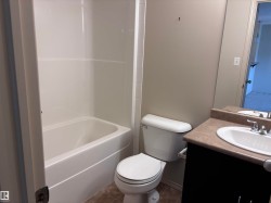 Bathroom featuring a white bathtub and shower surround, a white toilet, a dark wood-finish vanity with a light countertop, and a white drop-in sink with a chrome faucet - 