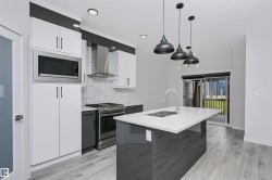 Kitchen featuring a central island with an undermount double sink, stainless steel appliances, white and gray cabinetry, and light wood-finish flooring - 