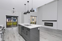 Open-concept living space featuring a central kitchen island with a double sink, stainless steel appliances, and pendant lighting - 