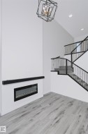 Vaulted ceiling with a geometric chandelier, electric fireplace, wood-finish flooring, and a staircase featuring black metal railings - 