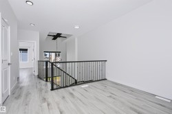 Upper-level landing featuring wood-finish flooring, recessed lighting, and a modern black metal railing - 