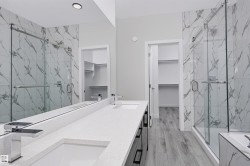 Modern bathroom featuring a dual vanity with rectangular sinks and chrome faucets, a frameless glass shower enclosure with marble-patterned tile, and light wood-finish flooring - 