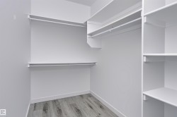 Walk-in closet with integrated white shelving, multiple hanging rods, and wood-finish flooring - 