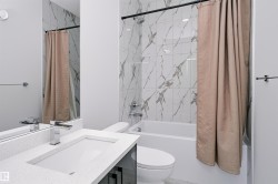 Contemporary bathroom featuring a built-in tub with marble-patterned tile surround, a built-in vanity with a stone-finish countertop, an undermount sink, and a chrome faucet - 