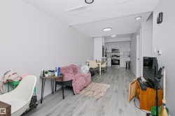 Open-concept living area featuring light wood-finish flooring, recessed lighting, and a modern kitchen with light grey cabinetry and stainless steel appliances - 