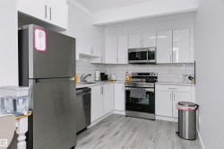 Contemporary kitchen featuring white shaker-style cabinetry, a white subway tile backsplash, stainless steel appliances, and light wood-finish flooring - 