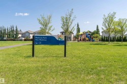 Expansive green space featuring a playground with colorful slides and climbing structures, mature trees, a paved walking path, and a Montrose Park sign - 