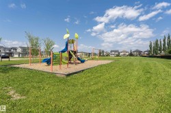Community park featuring a multi-component playground structure on wood chips, a swing set, and extensive green space - 