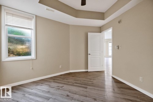 Room featuring wood-finish flooring, a tray ceiling, and a ceiling fan - #100 4835 104A St Nw, Edmonton, AB 