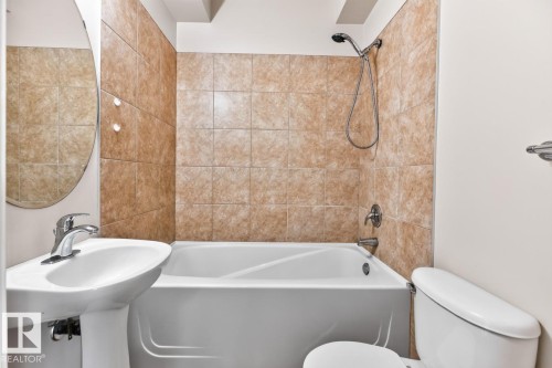 Bathroom featuring a pedestal sink, oval mirror, and a bathtub with a shower kit - #100 4835 104A St Nw, Edmonton, AB 