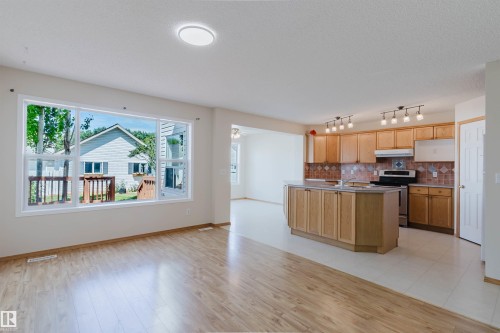 Open-concept interior featuring wood-finish flooring, a spacious kitchen island, extensive wood cabinetry, and a full tile backsplash - 1686 Tompkins Wynd Nw, Edmonton, AB - Indoor