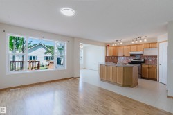 Open-concept interior featuring wood-finish flooring, a spacious kitchen island, extensive wood cabinetry, and a full tile backsplash - 