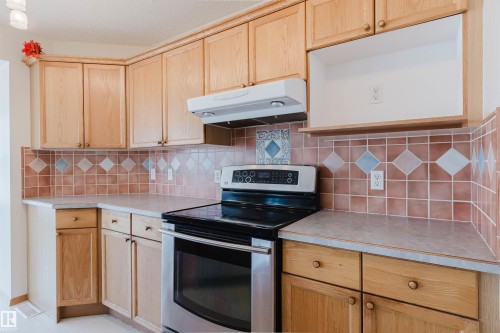 Kitchen featuring light wood cabinetry, a stainless steel range, and a tiled backsplash with decorative accents - 1686 Tompkins Wynd Nw, Edmonton, AB - Indoor Photo Showing Kitchen
