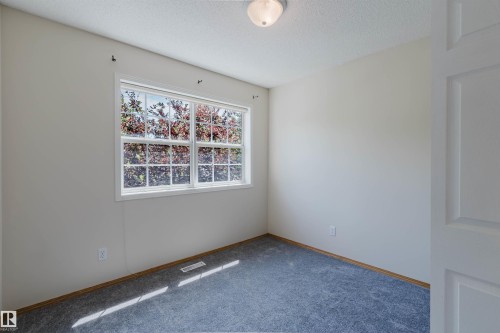 Bright room featuring a large window, neutral wall paint, gray carpet flooring, white trim, and a flush-mount ceiling light fixture - 1686 Tompkins Wynd Nw, Edmonton, AB - Indoor Photo Showing Other Room