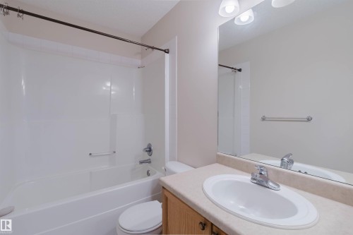 Bathroom featuring a built-in tub with an integrated shower, light-toned countertop, and a vanity with wood-finish cabinetry - 1686 Tompkins Wynd Nw, Edmonton, AB - Indoor Photo Showing Bathroom