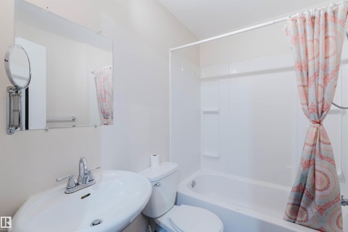 Bathroom featuring a white ceramic sink with chrome faucet, a wall-mounted mirror, and a full-size bathtub with an integrated shower - 1686 Tompkins Wynd Nw, Edmonton, AB - Indoor Photo Showing Bathroom