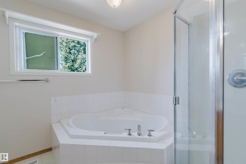 Corner soaking tub with tile surround, framed window, and glass-enclosed shower - 1686 Tompkins Wynd Nw, Edmonton, AB - Indoor Photo Showing Bathroom
