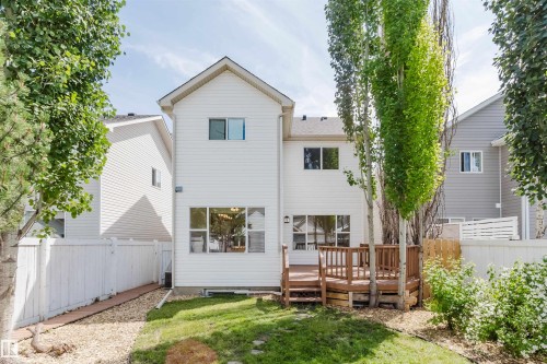 Two-story white siding residence featuring a multi-level wood deck, a partial grass yard, and a gravel-lined side yard - 1686 Tompkins Wynd Nw, Edmonton, AB - Outdoor