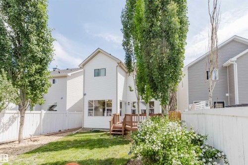 White siding exterior featuring a multi-level wood deck, a manicured lawn, and mature trees - 1686 Tompkins Wynd Nw, Edmonton, AB - Outdoor