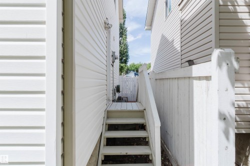 Exterior passageway featuring painted wood stairs, painted wood privacy fence, and white vinyl siding - 1686 Tompkins Wynd Nw, Edmonton, AB - Outdoor With Exterior