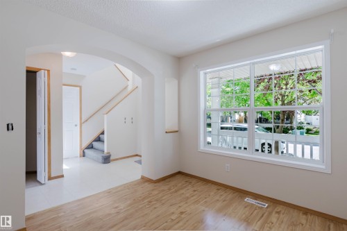Spacious interior featuring wood-finish flooring, a large multi-pane window, an arched entryway, light-colored walls, and a staircase with carpeted treads - 1686 Tompkins Wynd Nw, Edmonton, AB - Indoor Photo Showing Other Room