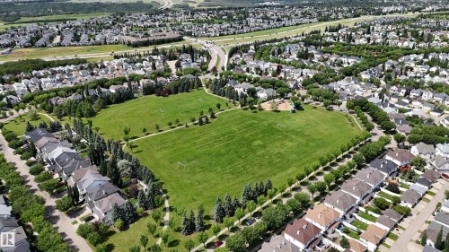 Expansive green space featuring large grassy areas, mature perimeter trees, and a visible play structure, surrounded by residential properties - 1686 Tompkins Wynd Nw, Edmonton, AB - Outdoor With View