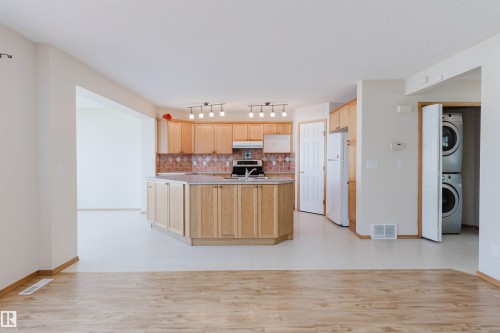 Open-concept kitchen featuring light wood cabinetry, a central island with a sink, a tile backsplash, and track lighting - 1686 Tompkins Wynd Nw, Edmonton, AB - Indoor Photo Showing Kitchen
