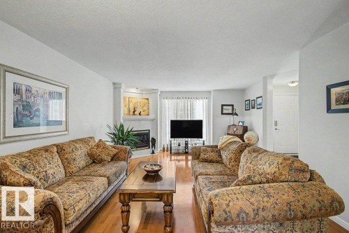 Spacious living area featuring wood-finish flooring, a corner fireplace, and ample natural light from the large window - #39 2419 133 Av Nw, Edmonton, AB - Indoor Photo Showing Living Room