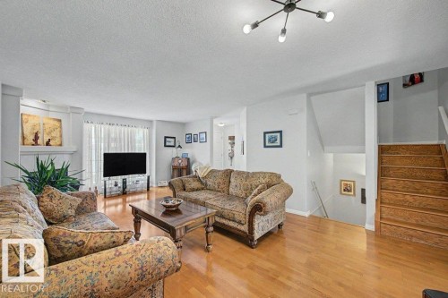 Spacious living area featuring wood-finish flooring, a contemporary ceiling light fixture, a white painted fireplace mantel, and a staircase with wood treads - #39 2419 133 Av Nw, Edmonton, AB - Indoor Photo Showing Living Room